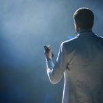 Photo features a man in a suit jacket speaking to a crowd. Giving speeches can be intimidating, but practice makes perfect. These four public speaking tips from Ken will help you wow any crowd.